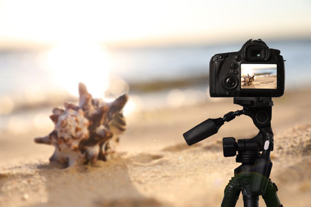 Taking photo of beautiful sandy beach and sea shell with camera mounted on tripodの写真素材