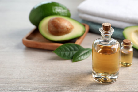 Bottles of essential oil, fresh avocado and towels on light wooden table, space for textの写真素材