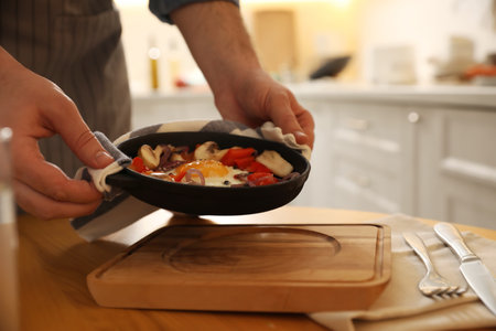 Man frying pan with fresh putting egg and vegetables on wooden board, closeupの写真素材