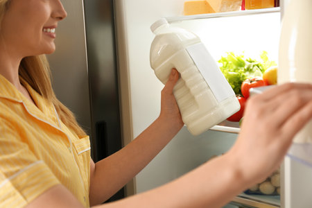 Young woman putting gallon of milk into refrigerator indoors, closeupの写真素材