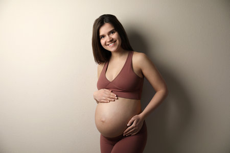 Pregnant young woman touching belly on beige backgroundの写真素材