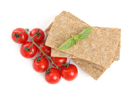 Crunchy rye crispbreads, fresh cherry tomatoes and basil on white background, top viewの写真素材