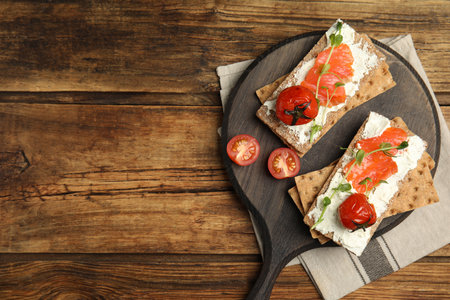 Fresh rye crispbreads with salmon, cream cheese and tomatoes on wooden table, top view. Space for textの写真素材