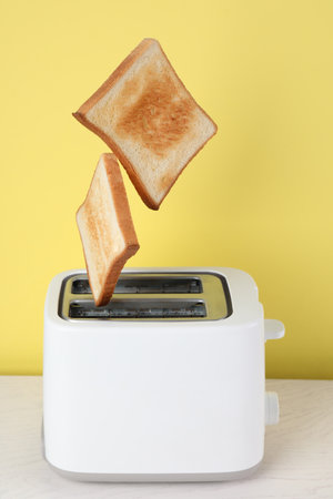 Bread slices popping up from modern toaster on white wooden tableの写真素材