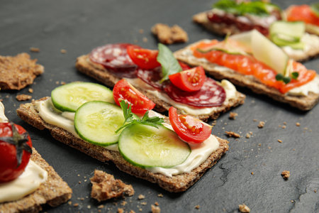 Fresh rye crispbreads with different toppings on black table, closeupの写真素材