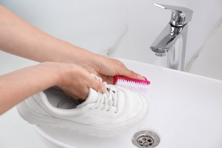 Woman washing shoe with brush under tap water in sink, closeupの写真素材