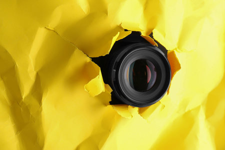 Hidden camera spying through torn hole in yellow paper, space for textの写真素材