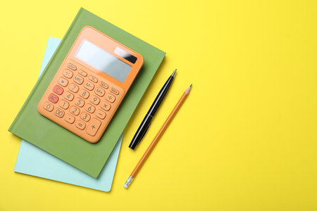 Calculator, notebooks, pen and pencil on yellow background, flat lay. Space for textの写真素材