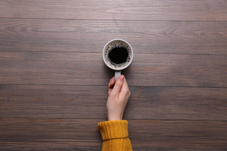 Woman with cup of coffee at wooden table, top viewの写真素材