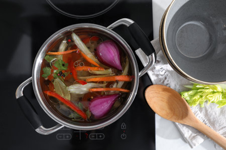 Kitchen counter with bowl, spoon and pot of delicious vegetable bouillon on stove, flat layの写真素材