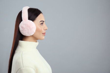 Beautiful young woman wearing earmuffs on light gray background. Space for textの写真素材
