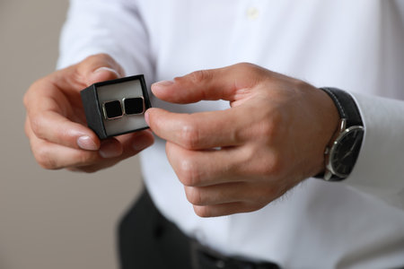 Stylish man holding box with cufflinks against beige background, closeupの写真素材