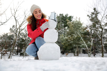 Young woman making snowman outdoors on winter day. Space for text