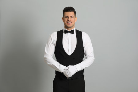 Handsome butler in elegant uniform on gray background