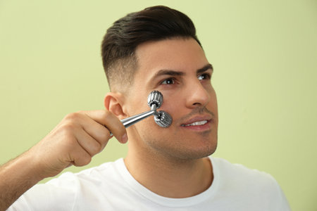 Man using metal facial roller on green backgroundの写真素材
