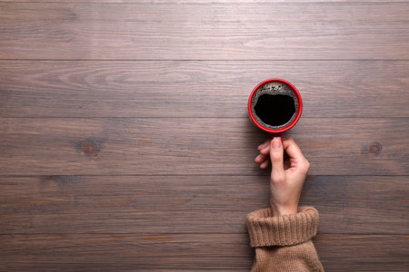 Woman with cup of coffee at wooden table, top view. Space for textの写真素材