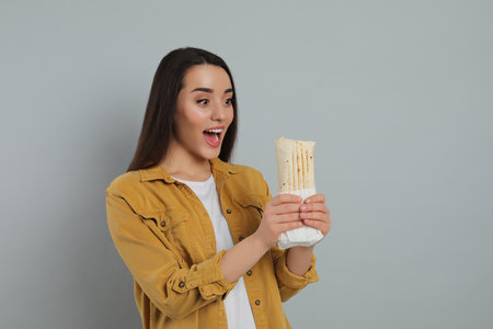 Happy young woman holding tasty shawarma on gray backgroundの写真素材
