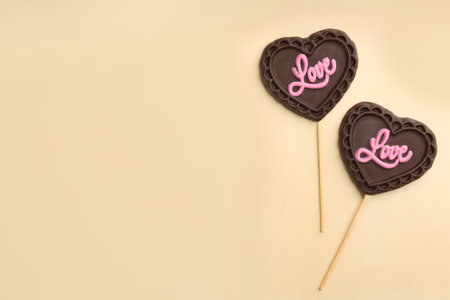Chocolate heart shaped lollipops with word Love on beige background, flat lay. Space for textの写真素材