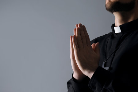 Priest praying on gray background, closeup. Space for textの写真素材