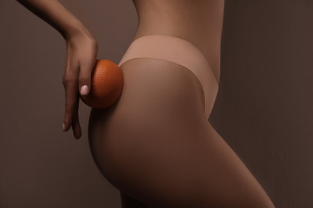 Closeup view of slim woman in underwear with orange on beige background. Cellulite problem conceptの写真素材