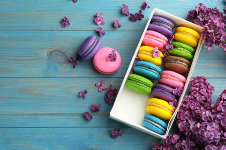 Delicious colorful macarons and flowers on light blue wooden table, flat lay. Space for textの写真素材