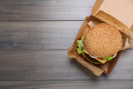 Delicious burger in cardboard box on wooden table, top view. Space for textの写真素材