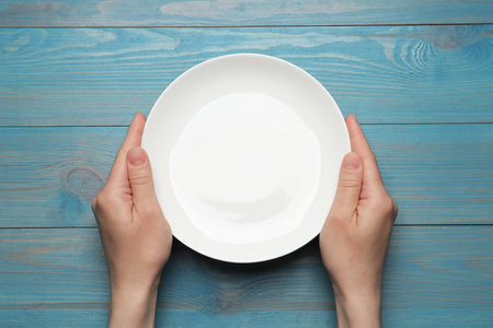 Woman with empty plate at blue wooden table, top viewの写真素材
