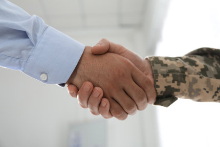 Soldier and businessman shaking hands indoors, closeupの写真素材