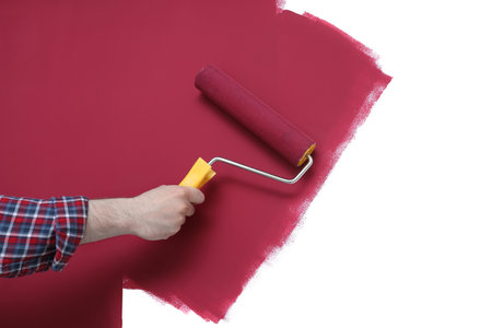 Man applying burgundy paint with roller brush on white wall, closeupの写真素材
