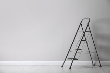 Modern metal stepladder near white wall indoors. Space for textの写真素材