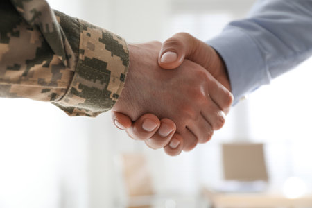 Soldier and businessman shaking hands indoors, closeupの写真素材