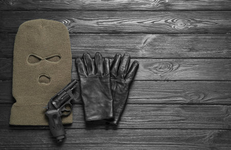 Beige knitted balaclava, gloves and gun on gray wooden table, flat lay. Space for textの写真素材