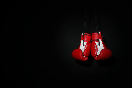 Pair of red boxing gloves hanging on black background, space for textの写真素材
