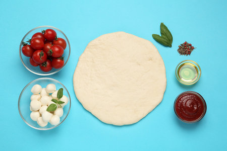 Raw dough and other pizza ingredients on light blue background, flat lay. Space for textの写真素材