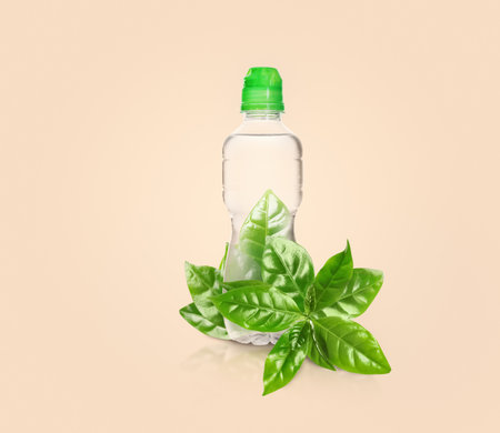 Bottle made of biodegradable plastic and green leaves on beige backgroundの写真素材