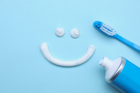 Funny face made with toothpaste, brush and tube on light blue background, flat layの写真素材
