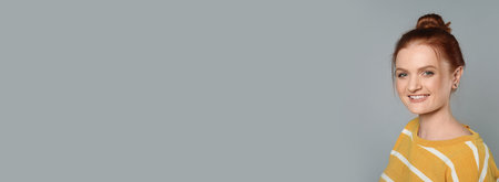 Candid portrait of happy red haired woman with charming smile on gray background, space for text. horizontal banner designの写真素材