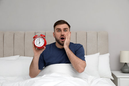Emotional overslept man with alarm clock in bed. Being late conceptの写真素材