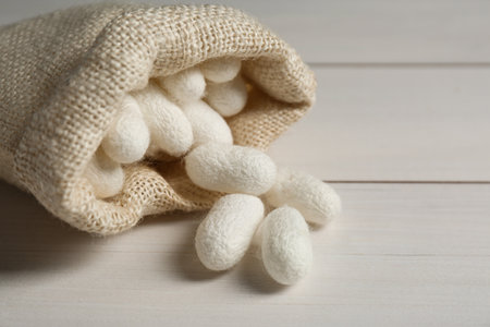 Silk cocoons with sackcloth bag on white wooden table, closeupの写真素材