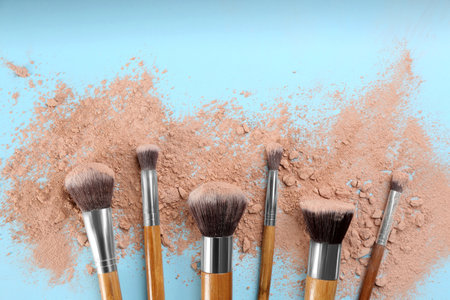 Brushes and scattered face powder on light blue background, flat layの写真素材
