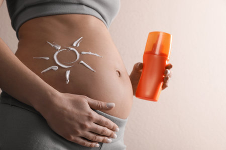 Pregnant woman with sun protection cream on beige background, closeupの写真素材