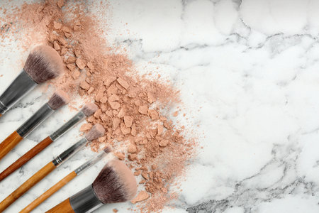 Makeup brushes and scattered face powder on white marble table, flat lay. Space for textの写真素材