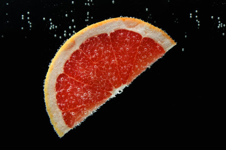 Slice of grapefruit in sparkling water on black background. Citrus sodaの写真素材