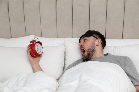 Emotional overslept man with alarm clock in bed, above view. Being late conceptの写真素材