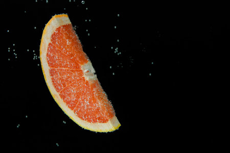 Slice of grapefruit in sparkling water on black background, space for text. Citrus sodaの写真素材