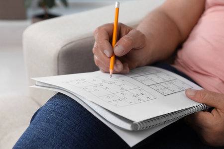 Senior man solving sudoku puzzle on sofa at home, closeupの写真素材