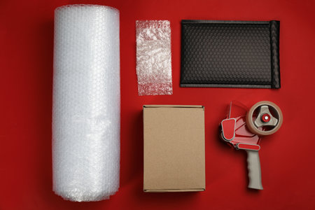 wrap with cardboard box, padded envelope and tape dispenser on red background, flat layの写真素材