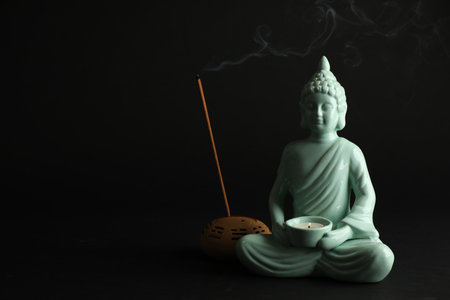 Beautiful ceramic Buddha sculpture with burning candle and incense stick on black background. Space for textの写真素材
