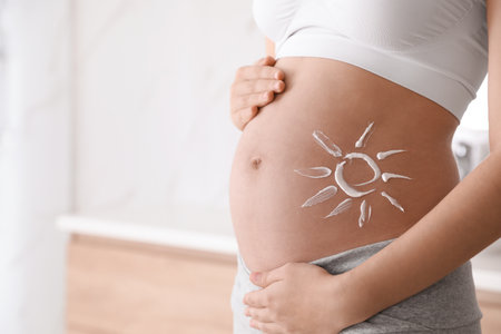 Young pregnant woman with sun protection cream on belly indoors, closeup. Space for textの写真素材