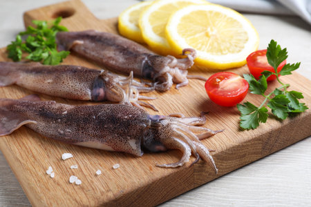Fresh raw squids with lemon, parsley and tomato on white wooden table, closeupの写真素材